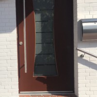 Rotbraune moderne Haustür mit vertikalem, taillierten Glaseinsatz sowie senkrechtem Edelstahl-Stangengriff. Rotbraune moderne Haustür mit vertikalem, taillierten Glaseinsatz sowie senkrechtem Edelstahl-Stangengriff.
